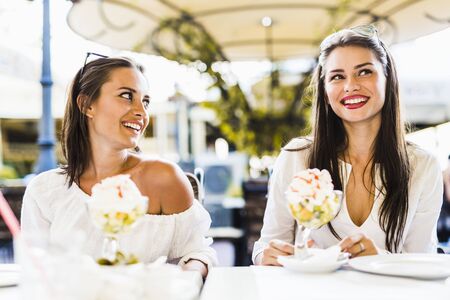 Two beautiful young women smiling and having a fruit salad in a restaraunt outdoorsの写真素材