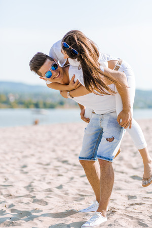 Cheerful handsome man carrying his girlfriend on his back on the beachの写真素材