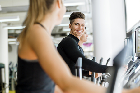 Handsome man and beautiful young woman using a stepper in a gym and having a conversationの写真素材
