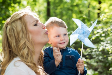 Beautiful woman holding her son in the blowing paper windmillの写真素材