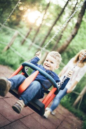 Mother and child outdoors in playground riding a  swing and smilingの写真素材