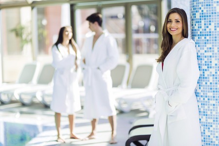 Friends dressed in bathrobes relaxing in a spa next to a swimming pool