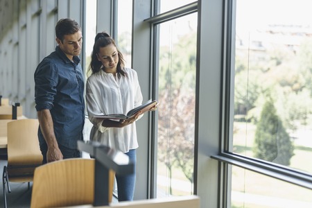 Two  smart students reading and studying in library whole searching through books on the shelvesの写真素材