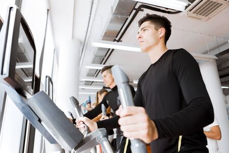 Young healthy group of people working out on a elliptic trainer in a fitness center