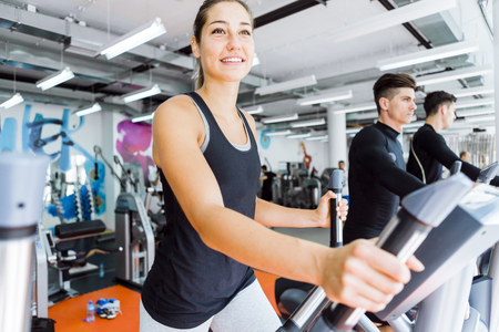 Young fit woman using an elliptic trainer in a fitness center and smiling