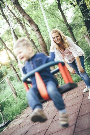 Mother and child outdoors in playground riding a  swing and smilingの写真素材