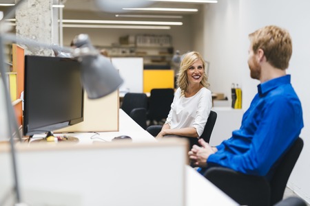 Beautiful blonde sitting in an office and working and talking with a colleagueの写真素材