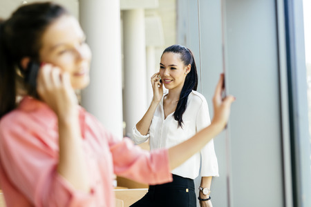 Beautiful women, colleagues using phones and talkin during breakの写真素材