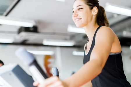 Beautiful young lady using the elliptical trainer in a gym in a positive moodの写真素材