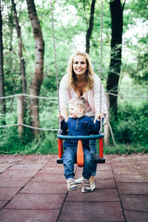Mother and child outdoors in playground riding a  swing and smilingの写真素材
