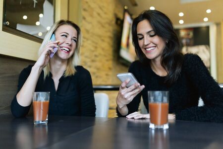 Two beautiful women talking on phone in cafe while being happy