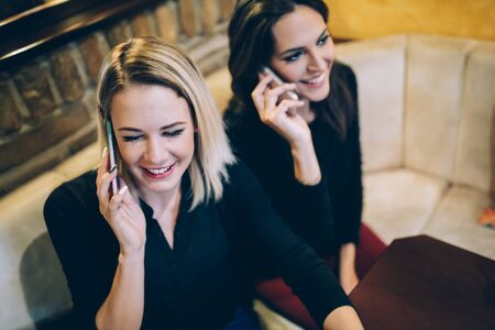 Two beautiful women talking on phone in cafe while being happyの写真素材