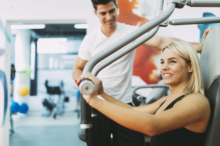 Beautiful woman exercising in gym with some help by personal trainer
