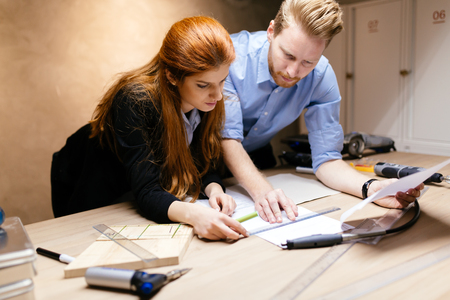 Creative designers working in workshop while standing at the desk full of tools and discussing ideasの写真素材