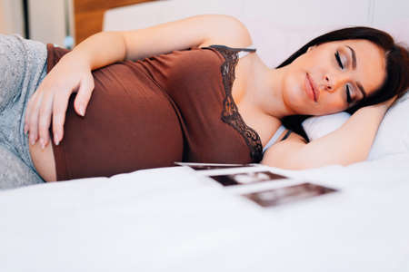 Beautiful pregnant woman resting with ultrasound scan being next to herの写真素材