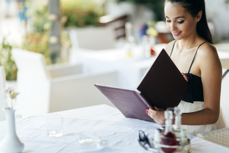 Beautiful woman ordering from menu in restaurantの写真素材