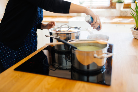 Beautiful woman adding spices to food while cooking in kitchenの写真素材