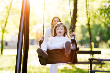 Disabled child enjoying the swing outdoors with sisterの写真素材