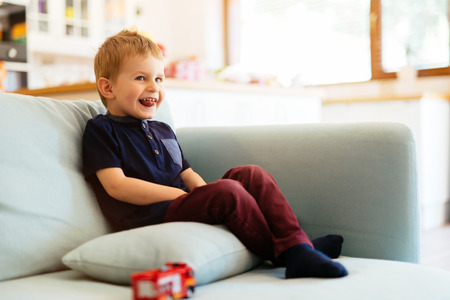 Happy boy sitting on sofa in living roomの写真素材