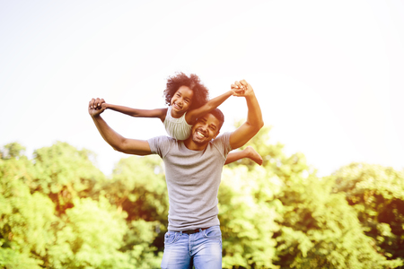 Child flying on father shoulders while held piggybackの写真素材