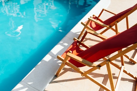 Deck chairs at side of pool symbolizing summer vacation