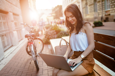 Female student using laptop outdoors and studyingの写真素材