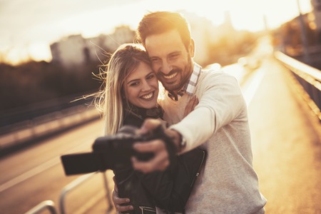 Happy couple taking selfies in city during sunsetの写真素材