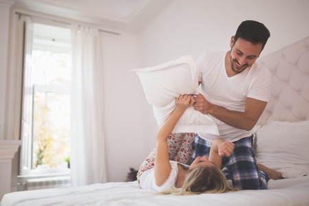 Beautiful couple pillow fighting and smilingの写真素材
