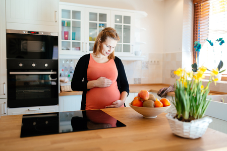 Beautiful pregnant woman in kitchen holding her bellyの写真素材