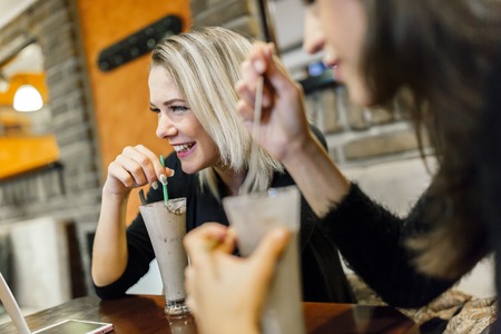 Two women drinking and talking in cafe while having a good timeの写真素材