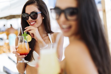 Beautiful women on sunny beach enjoying cocktailsの写真素材
