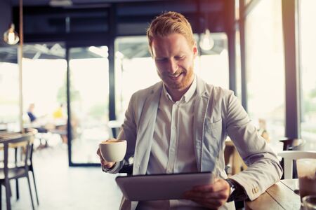 Busy businessman on coffee break using tabletの写真素材