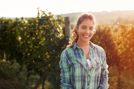 Happy woman in vineyard checking grapes before harvestingの写真素材