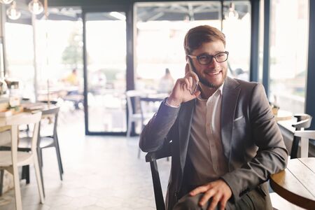 Businessman wearing glasses talking on phone in cafeの写真素材