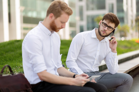 Business colleagues sitting on bench outdoors and talkingの写真素材