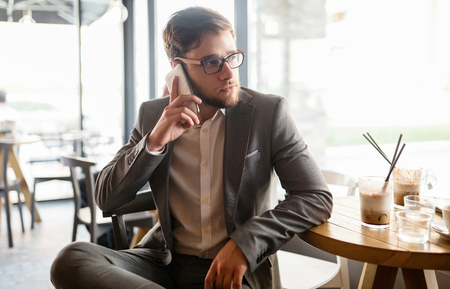 Businessman wearing glasses talking on phone in cafeの写真素材