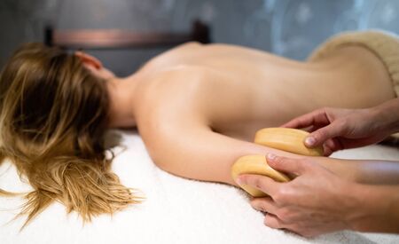 Massage therapist using wooden tool to massage patient in saloonの写真素材