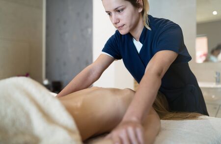Masseur massaging back of female in spa resortの写真素材
