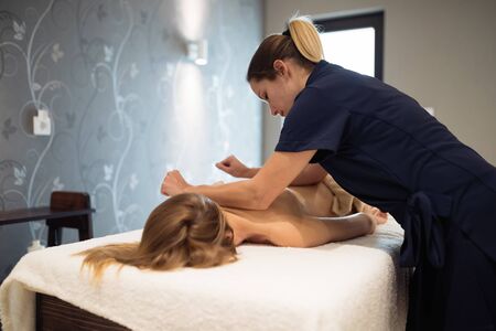 Masseur massaging back of female in spa resortの写真素材