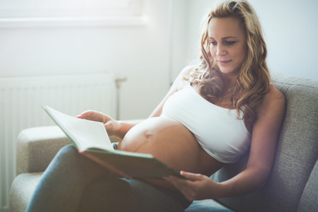 Beautiful pregnant woman reading book to baby in tummyの写真素材