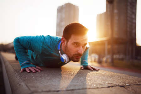 Handsome man fitness exercising by doing push ups in sunsetの写真素材