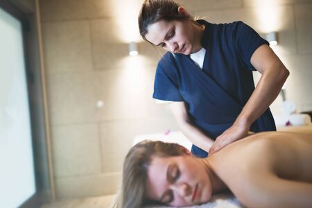 Masseur massaging back of female in spa resortの写真素材