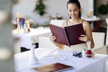 Beautiful woman ordering from menu in restaurant and deciding what to eatの写真素材