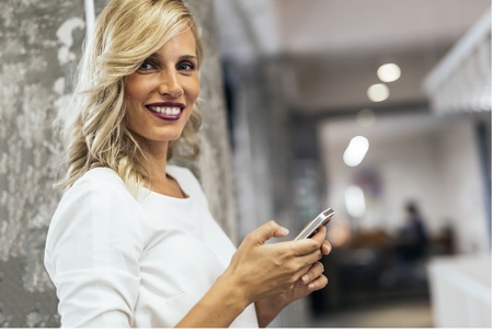 Beautiful blonde woman in modern office using phoneの写真素材