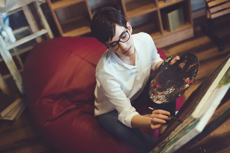 Female artist painting with palette and paintbrush on canvasの写真素材