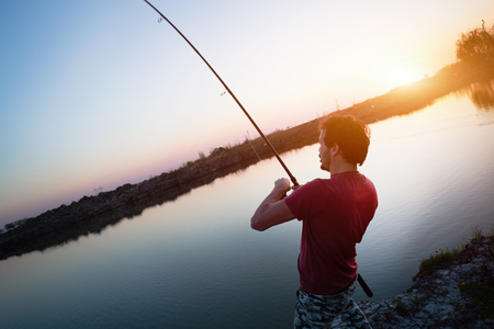 Young man fishing on lake at sunset enjoying hobbyの写真素材