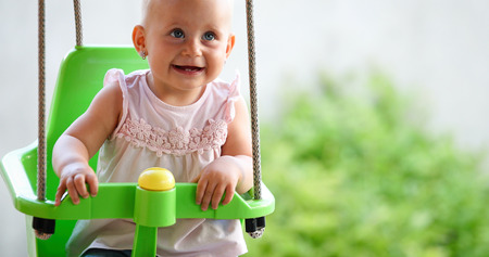 Happy baby enjoying outdoor activities and smiling while swingingの写真素材