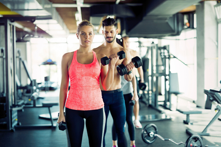Personal trainer helping young woman with exercises for bicepsの写真素材