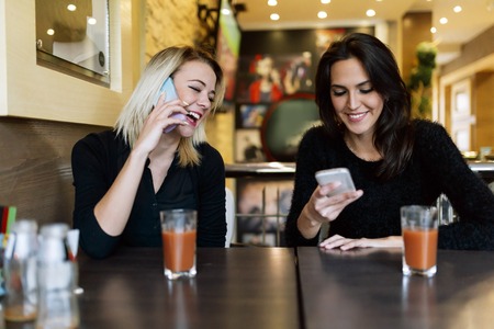 Two beautiful women talking on phone in cafeの写真素材