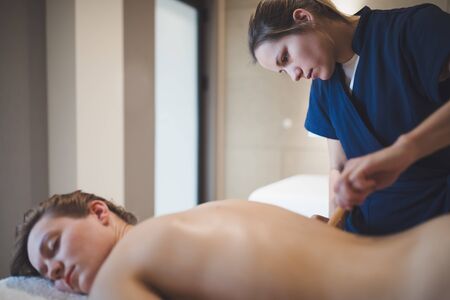 Massage therapist using wooden tool to massage patient
